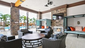 An outdoor patio area with wicker furniture, a round table, and a fireplace. - 7BR Resort Pool Home Near Disney - 8004 (Davenport)