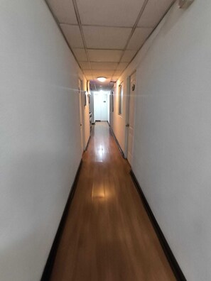 A long, narrow hallway with wooden flooring and white walls. - Hotel Dakota  (Antofagasta)
