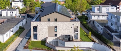 En moderne boligbygning med saddeltag, store vinduer og en anlagt forhave.