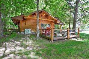 A wooden cabin with a porch, a table, and chairs, surrounded by trees. - Cozy King Suite, Perfect Base for Trail & Lake Fun (Cable)