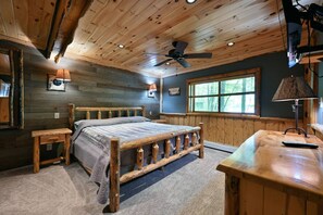 A wooden cabin bedroom with a bed, a desk, a ceiling fan, and a window. - Cozy King Suite, Perfect Base for Trail & Lake Fun (Cable)