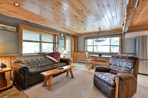 Ein gemütliches Blockhaus-Interieur mit Holzboden, einer Couch, einem Sessel, einem Esstisch und einem Kühlschrank.