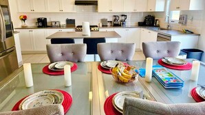 A modern kitchen with white cabinets, a central island with seating, and a dining area with a glass table and grey upholstered chairs. - Lola's Place Luxury 4BR with 4BEDS  Close to fall, sleeps 8... (Welland)