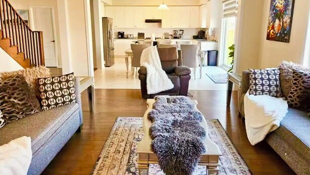 A modern living room with a sofa, a coffee table, and a rug. There is a staircase on the left and a kitchen in the background. - Lola's Place Luxury 4BR with 4BEDS  Close to fall, sleeps 8... (Welland)