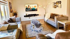 A living room with a flat-screen TV mounted on the wall, a sofa, a coffee table, and a rug. - Lola's Place Luxury 4BR with 4BEDS  Close to fall, sleeps 8... (Welland)