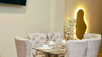 A dining area with a round table, six upholstered chairs, and a wall-mounted TV.