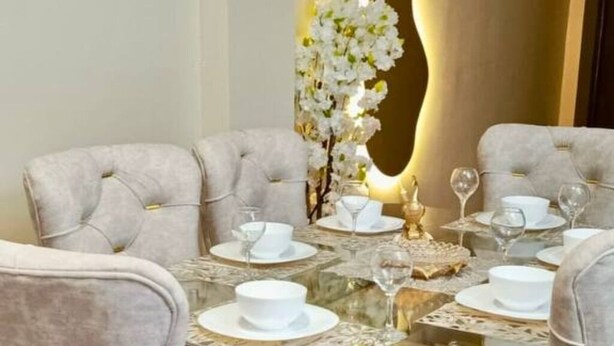 A dining table with six chairs, white tableware, and a vase of white flowers.