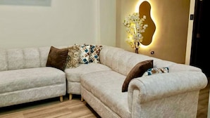 A L-shaped sectional sofa with patterned cushions, a wall-mounted light fixture, and a wooden floor.