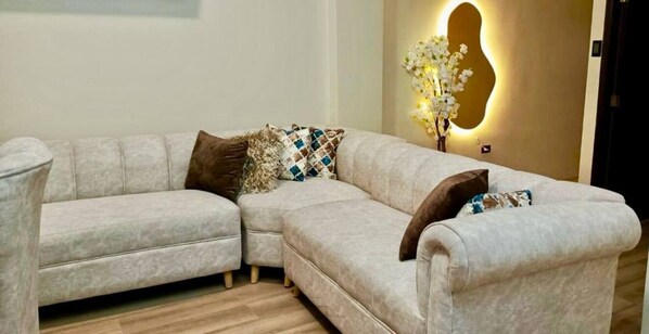 A L-shaped sectional sofa with patterned cushions, a wall-mounted light fixture, and a wooden floor. - CABALLITO DE MAR (Puerto Baquerizo Moreno)