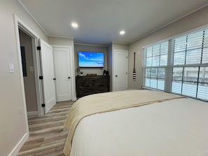 Un dormitorio con una cama grande, un aparador, un televisor y una ventana con persianas.