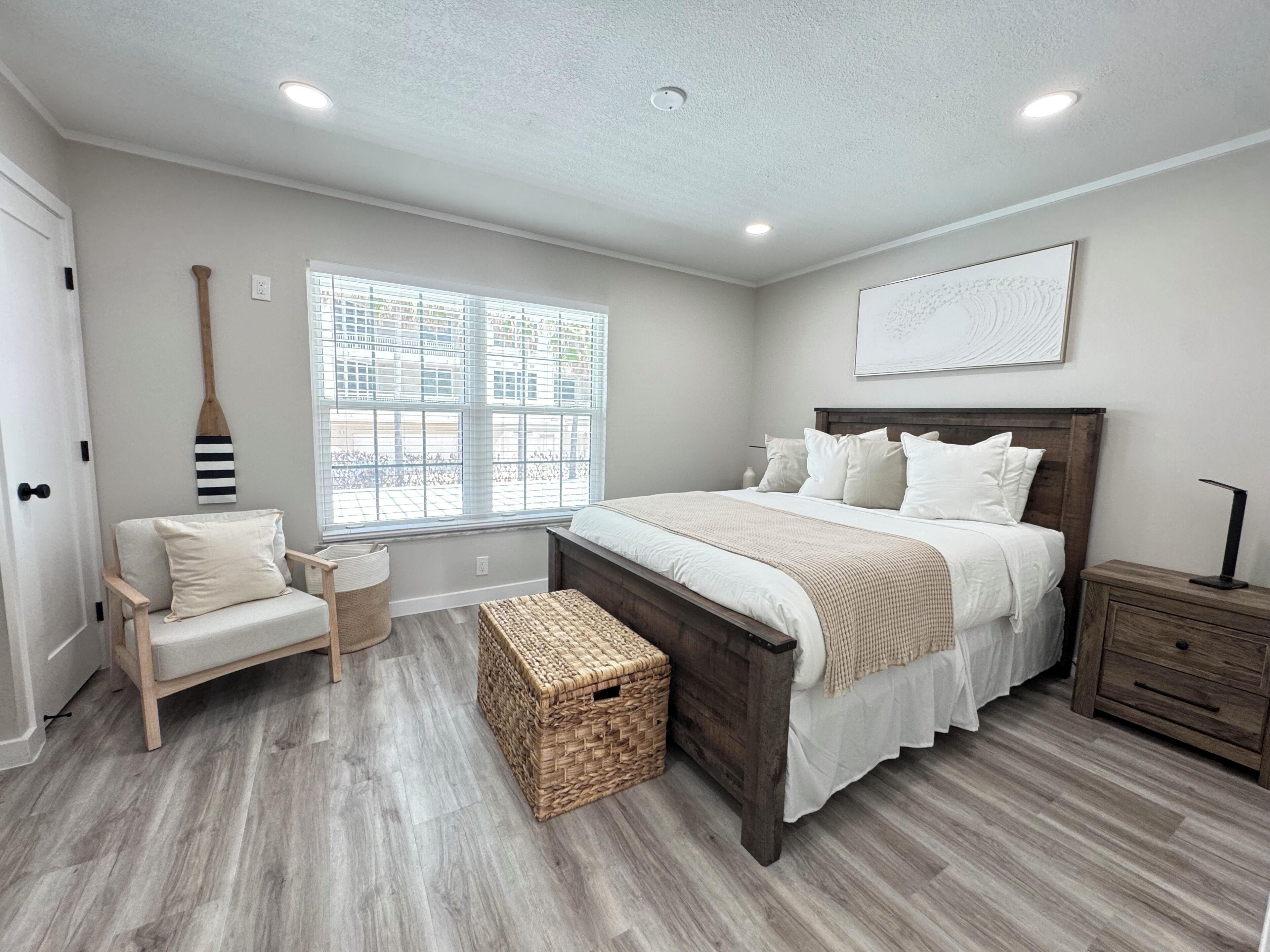 A bedroom with a bed, a chair, a nightstand, a window with blinds, and a ceiling light.