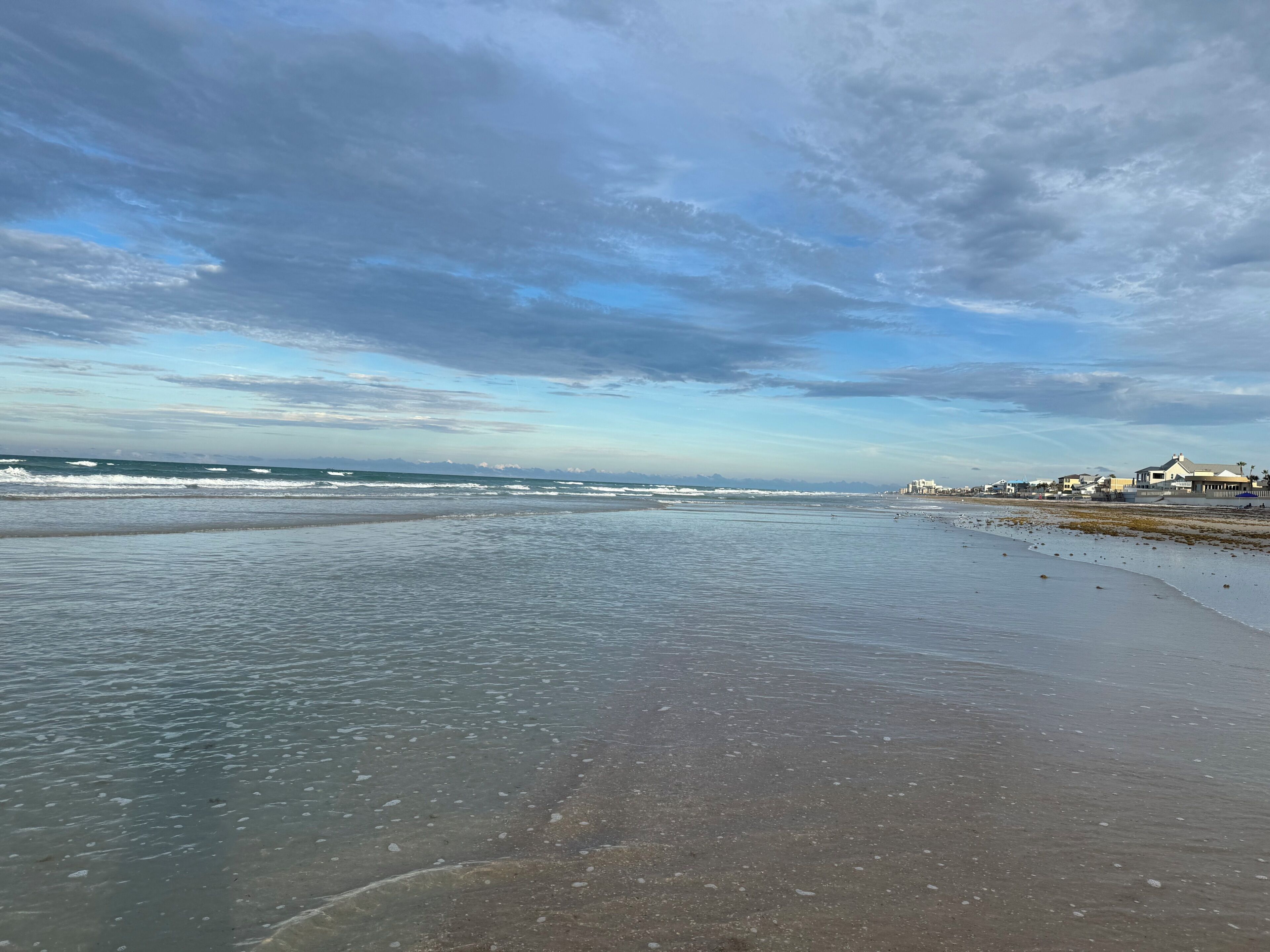 A beach with waves, a clear sky, and buildings in the distance.