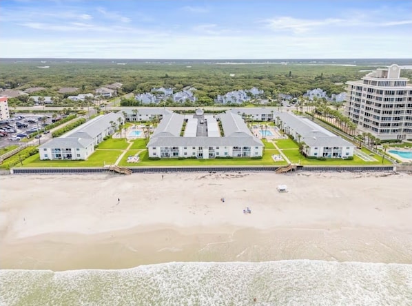 Un hotel frente a la playa con varias edificaciones, una playa arenosa y una vista despejada del océano.