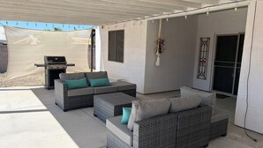 Un espacio de patio al aire libre con mobiliario de mimbre, una parrilla y una planta colgante.