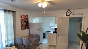 Habitación pequeña con cama, una mesa de comedor y sillas, kitchenette y una puerta que da a otra habitación.