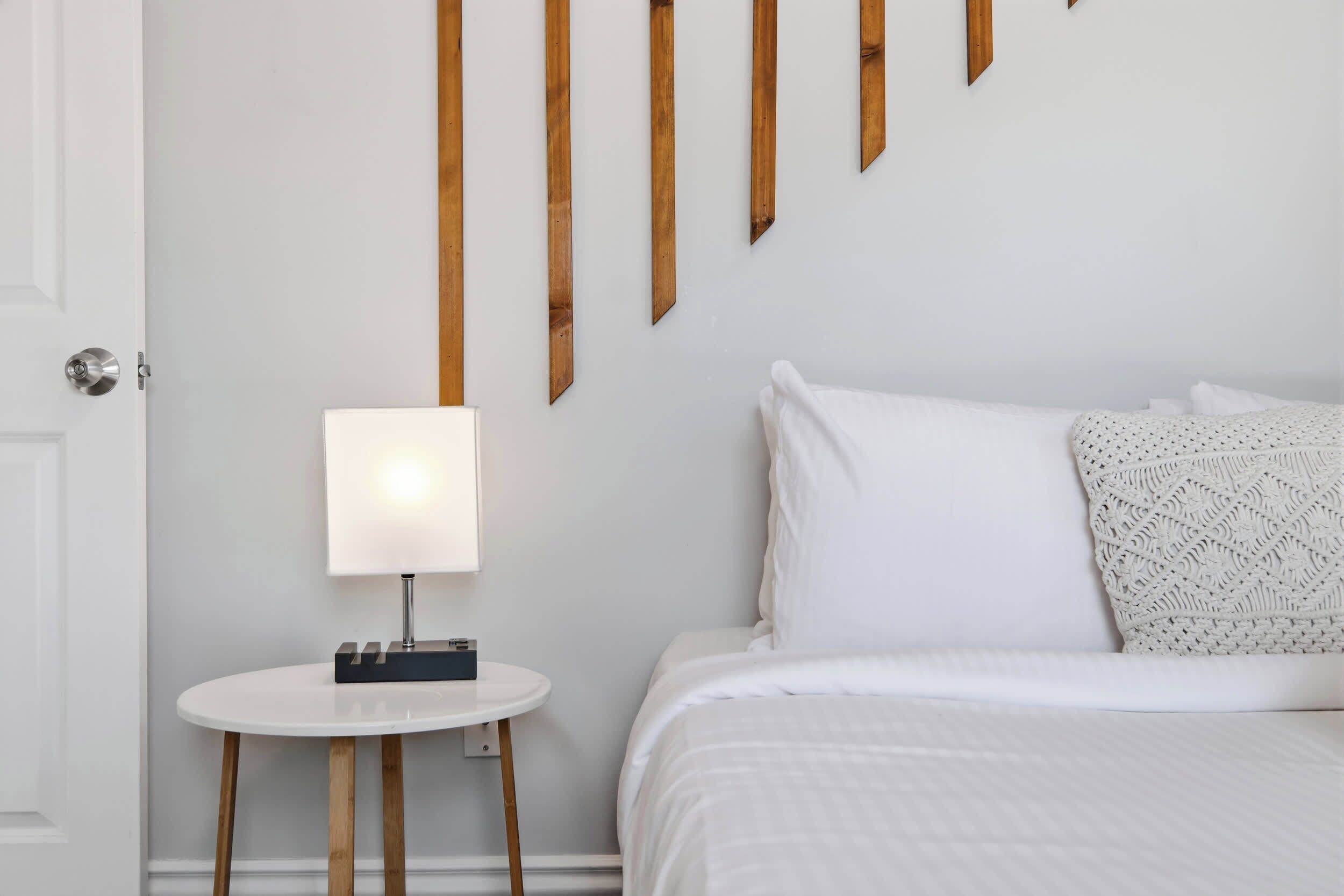 A neatly arranged hotel room with a bed, a bedside table with a lamp, and wooden slats on the wall.