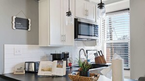 A modern kitchen with white cabinets, a microwave, a toaster, and a coffee maker. There's a basket with a plant and a roll of paper towels on the counter.
