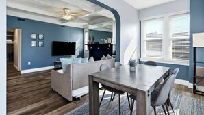 A modern living room with a grey sofa, a dining table, and a flat-screen TV.