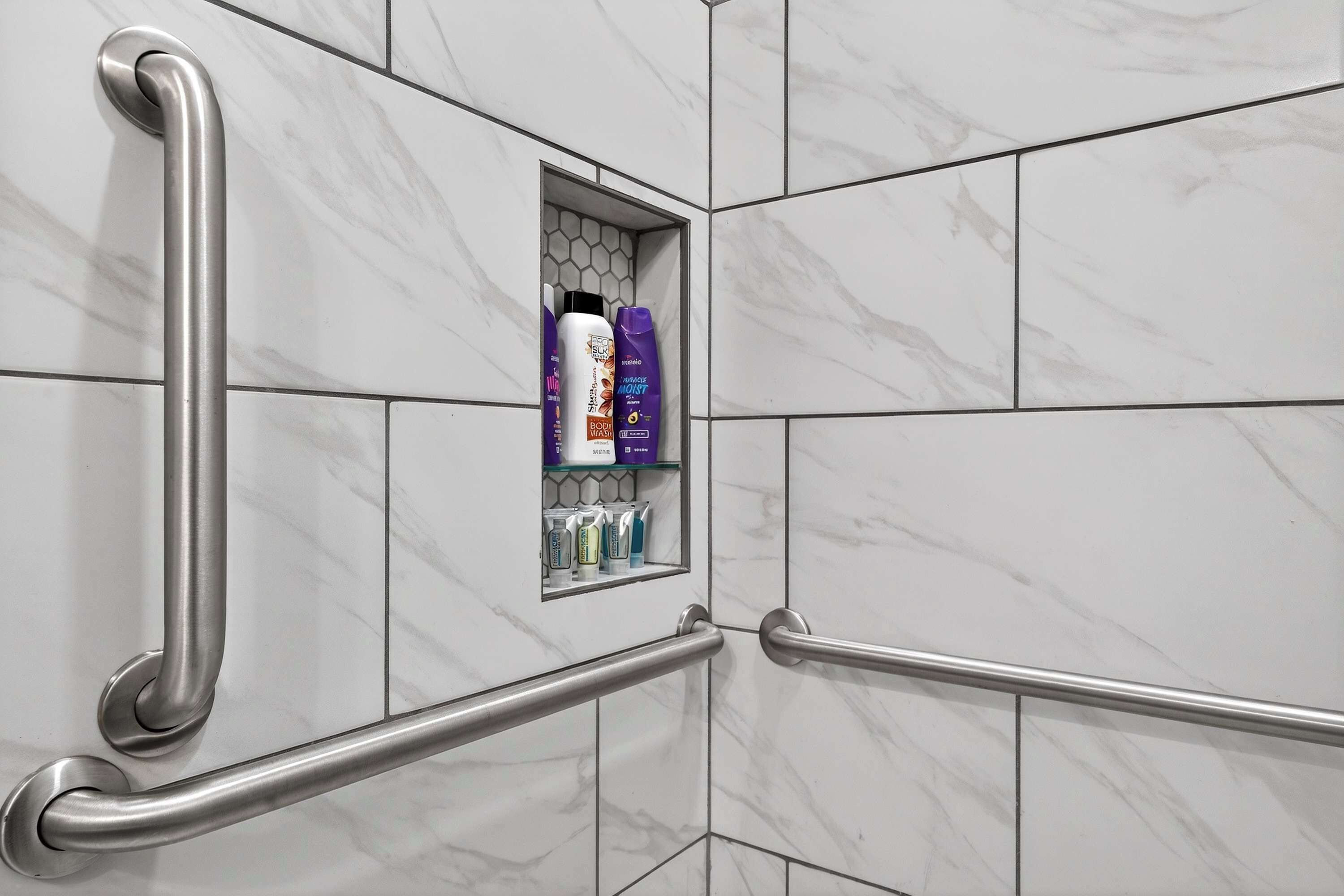 A bathroom with a handrail, a shelf with toiletries, and a marble wall.