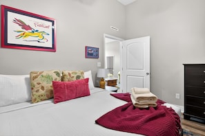 Un letto rifatto con cuscini, una coperta rossa e un quadro appeso al muro.
