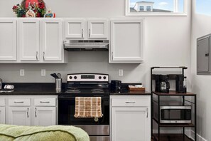 Una cucina con mobili bianchi, una stufa nera, un forno a microonde e una macchina da caffè.