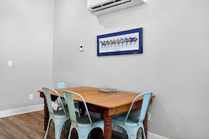 Zona pranzo con tavolo in legno e sedie azzurre, un quadro di un cavallo incorniciato sulla parete e un condizionatore d'aria sopra.