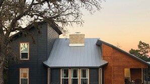 Una casa moderna de dos pisos con un amplio porche delantero, una chimenea de piedra y revestimiento de madera en tonos oscuros y claros.