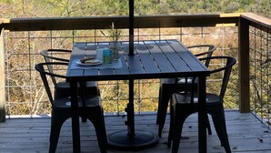 Una terraza de madera con una mesa y sillas bajo un paraguas grande, con vistas a un paisaje montañoso.