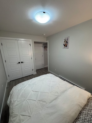 A bedroom with a bed, two white doors, a ceiling light, and a floral artwork on the wall. - Alake Villa (Saskatoon)