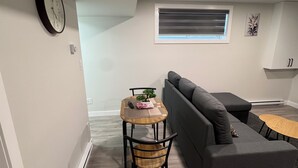 A modern living room with a grey sofa, a small wooden table with a plant, and a clock on the wall. - Alake Villa (Saskatoon)