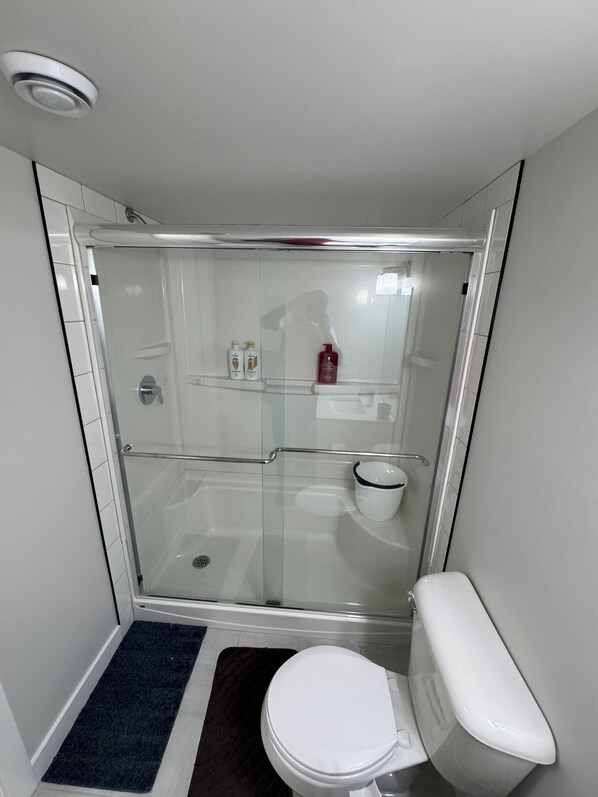 Une salle de bain moderne avec une douche à parois de verre, des toilettes blanches et une petite étagère contenant des articles de toilette.