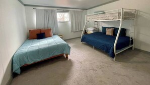 Une chambre avec deux lits, dont un lit simple et un lit superposé, un sol recouvert de moquette et une fenêtre avec des rideaux.