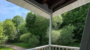 Une terrasse extérieure couverte, avec une table ronde et deux chaises, entourée d’une balustrade blanche.