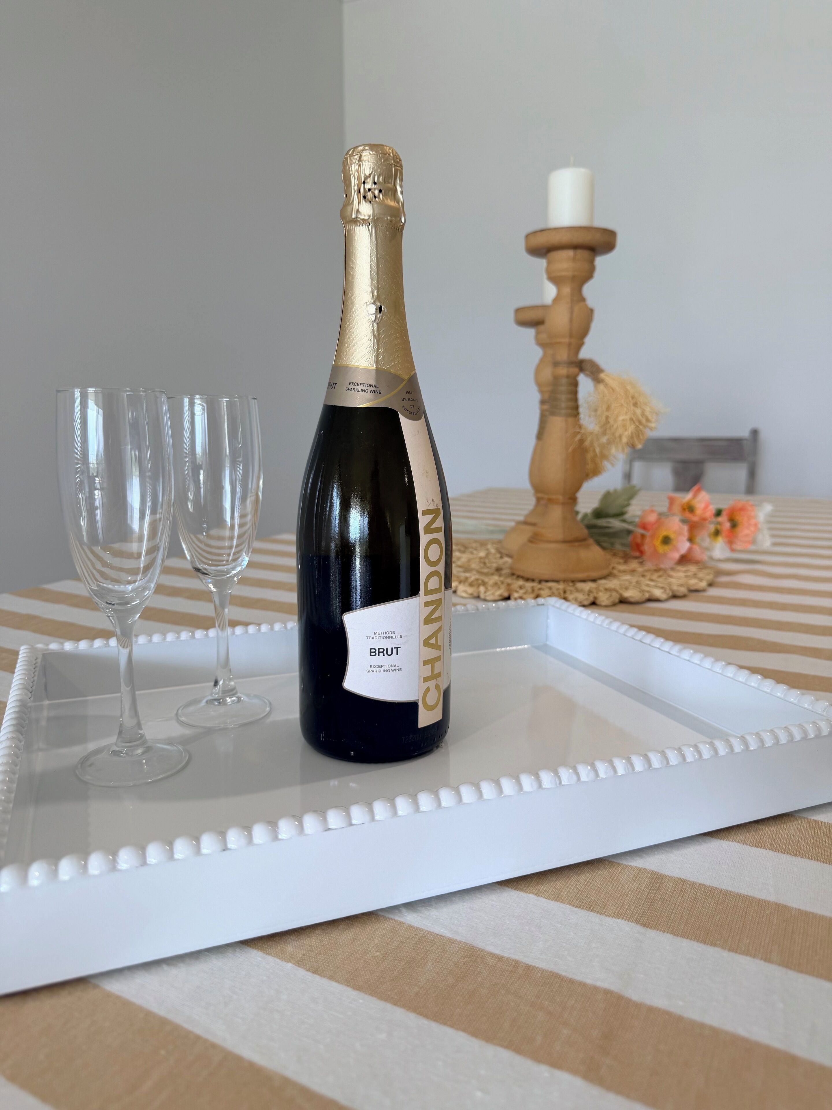 A bottle of Brut champagne on a white tray with two glasses beside it, set on a checkered tablecloth.