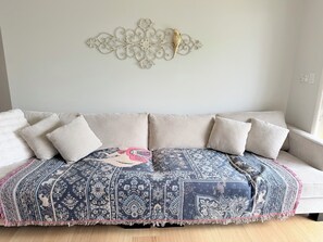 Un sofá con un plaid estampado, un adorno de pared y una ventana con persianas.