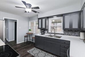 A modern kitchen with dark cabinets, a white countertop, a built-in sink, and a ceiling fan. - Spacious 3-bedroom house in charming East side neighborhood. (Wichita)