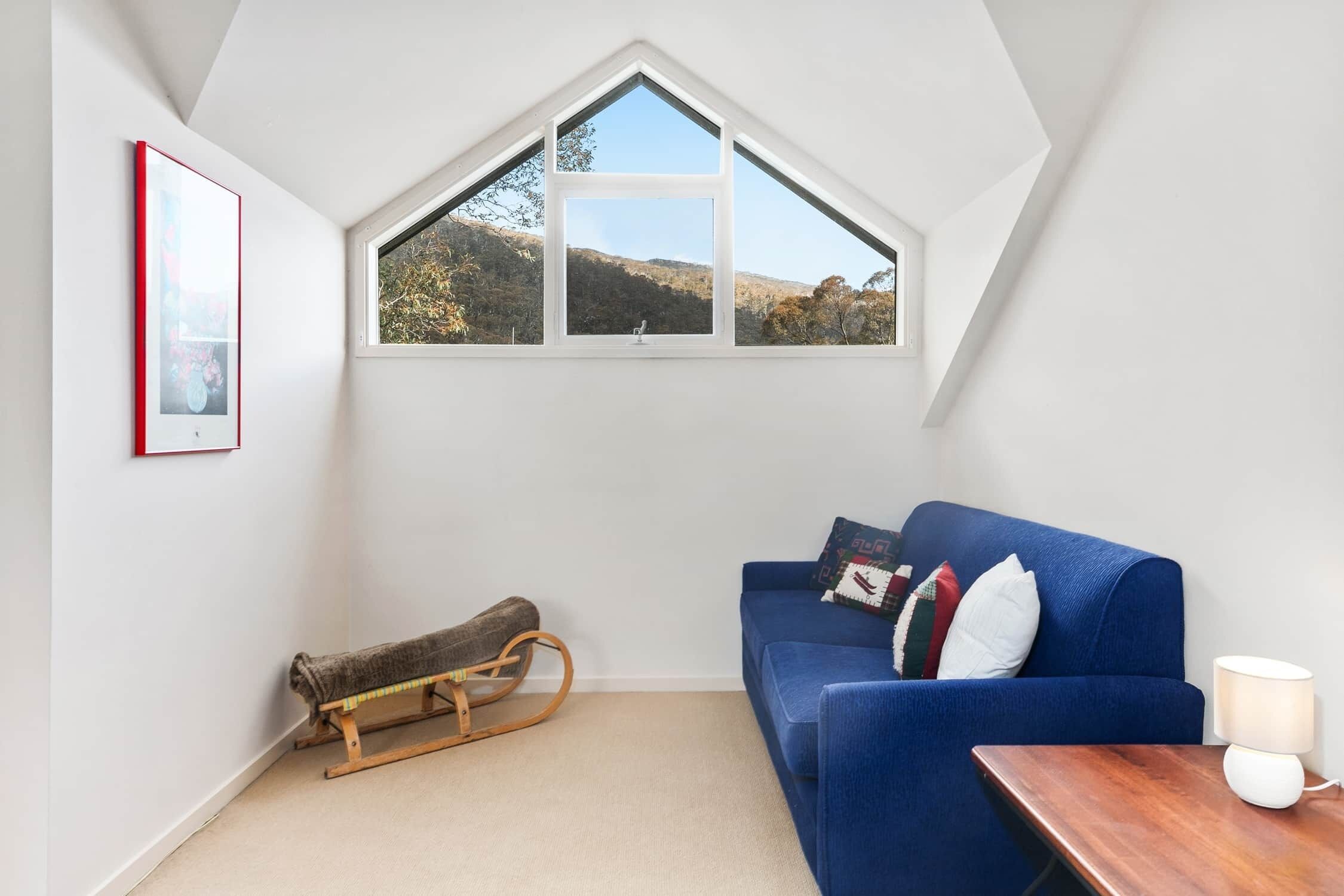 A cozy room with a sloped ceiling, a blue sofa, a wooden rocking chair, a small table with a lamp, and a framed picture on the wall.