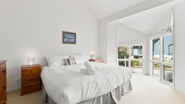 A bedroom with a large bed, wooden nightstands, a dresser, and a window with a view of greenery and buildings.