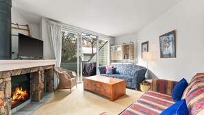 A living room with a stone fireplace, a television, a sofa, and a bookshelf.