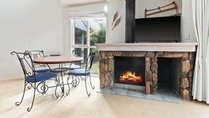 A stone fireplace with a fire, a dining table with chairs, and a TV mounted above the fireplace.