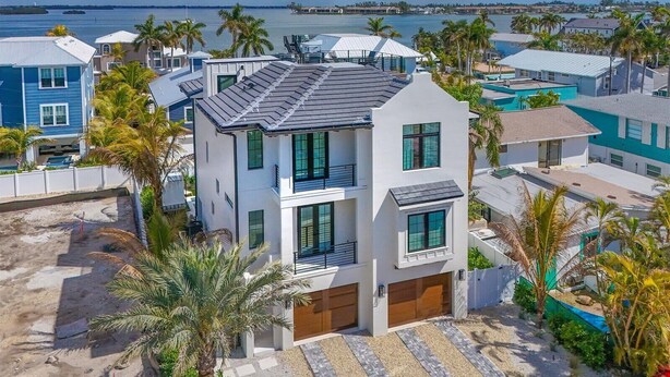 A modern two-story house with a garage, surrounded by palm trees and a view of the sea. - Seaside Serenity | Rooftop Views! (Bradenton Beach)