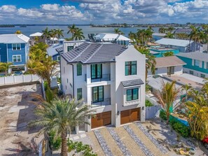 Una casa moderna de dos pisos con garaje, rodeada de palmeras y vista al mar.
