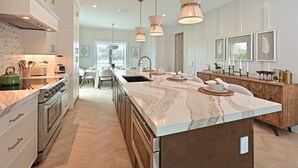 A modern kitchen with a large island, stainless steel appliances, and pendant lighting. - Seaside Serenity | Rooftop Views! (Bradenton Beach)
