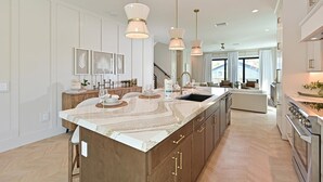 A modern kitchen with a large island, pendant lighting, and a view to the living area. - Seaside Serenity | Rooftop Views! (Bradenton Beach)