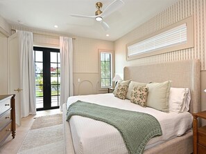 Un dormitorio con cama, ventilador de techo, ventana con persianas y vistas al exterior.