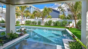 A swimming pool with a wooden ceiling, surrounded by lush greenery and a white fence. - Seaside Serenity | Rooftop Views! (Bradenton Beach)