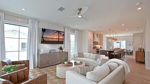A spacious living room with a large sectional sofa, a coffee table, and a TV mounted on the wall. There is a dining area with a kitchen in the background. - Seaside Serenity | Rooftop Views! (Bradenton Beach)
