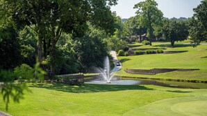 A golf course with a fountain, lush greenery, and a pond. - Stylish Branson Retreat with Golf and Amenities (Branson)