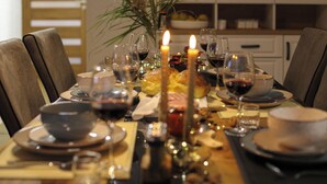 Une table à manger dressée avec des assiettes, des verres, des bougies et un saladier rempli de fruits.