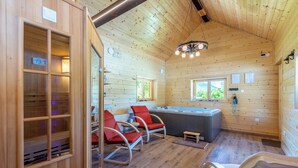 L’intérieur d’un chalet en bois comprend un sauna, des chaises rouges, un jacuzzi et un plafond en bois.
